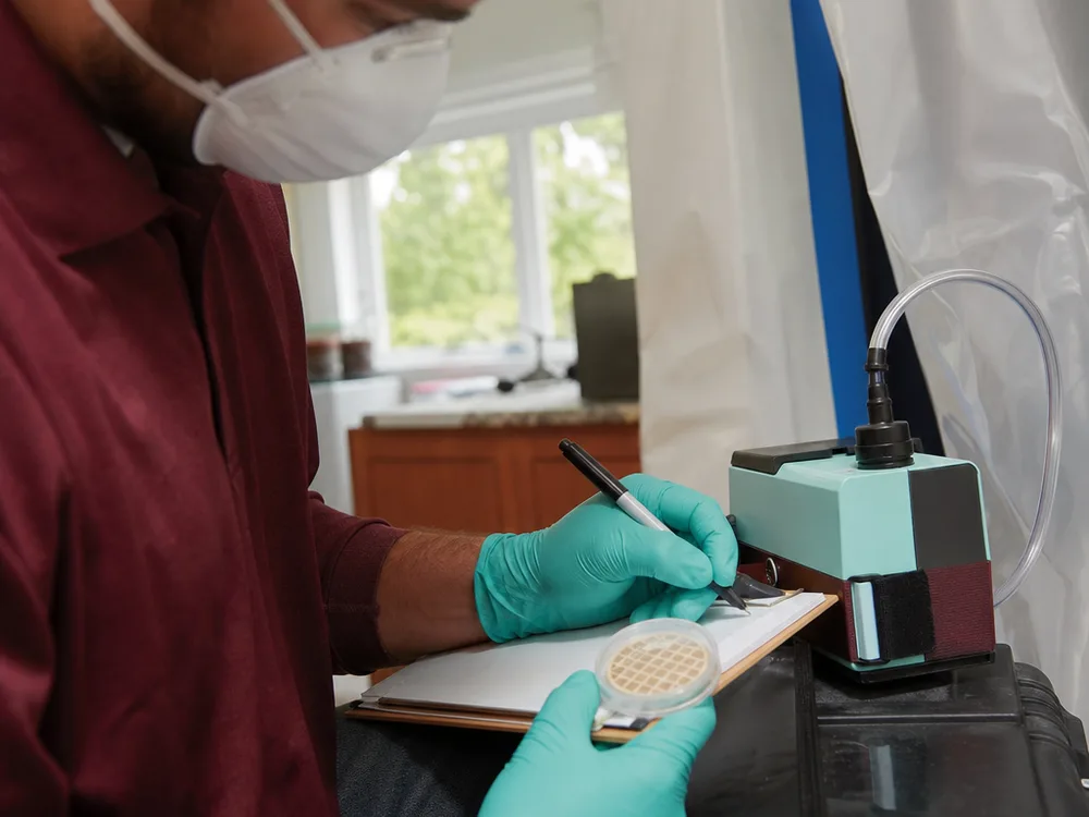 Contractor holding a calibrated air pump and spore trap cassette near breathing height in a living space
